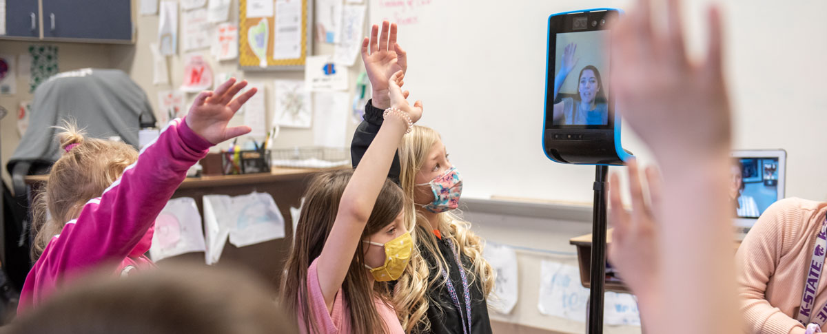 Students in a classroom interact with a virtual teacher.