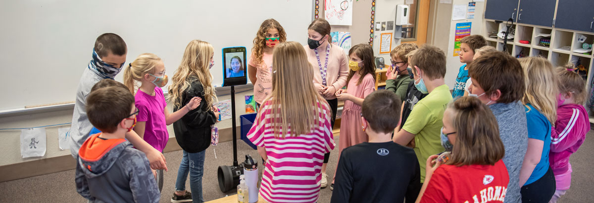 Students interact with a virtual teacher in a classroom. 