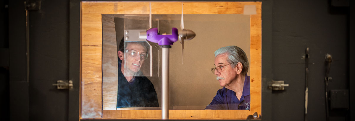 Engineers look at a wind tunnel. 