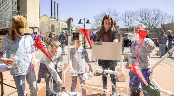 Children participating in a hands-on outdoor activity using funnels, pipes, and water to explore how water flows through a system.