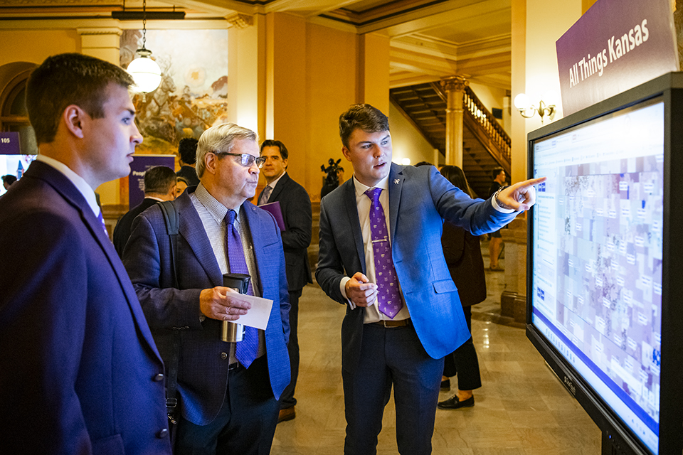 Parker Vulgamore talks to a group of men at the Kansas State Capitol and shows them an interactive map on a large portable screen.