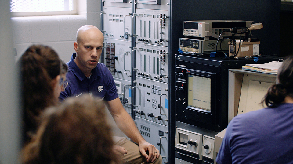 A professor in a purple polo goes over a display at a nuclear engineering control panel.