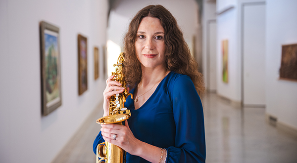 A college professor poses for a portrait while holding a saxophone in a museum hallway.