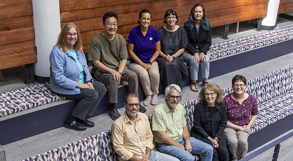 A group of a dozen college professors and researchers sit on risers and pose for a group portrait.