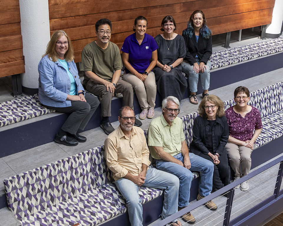 A group of college faculty sit on stairs and pose for a portrait.