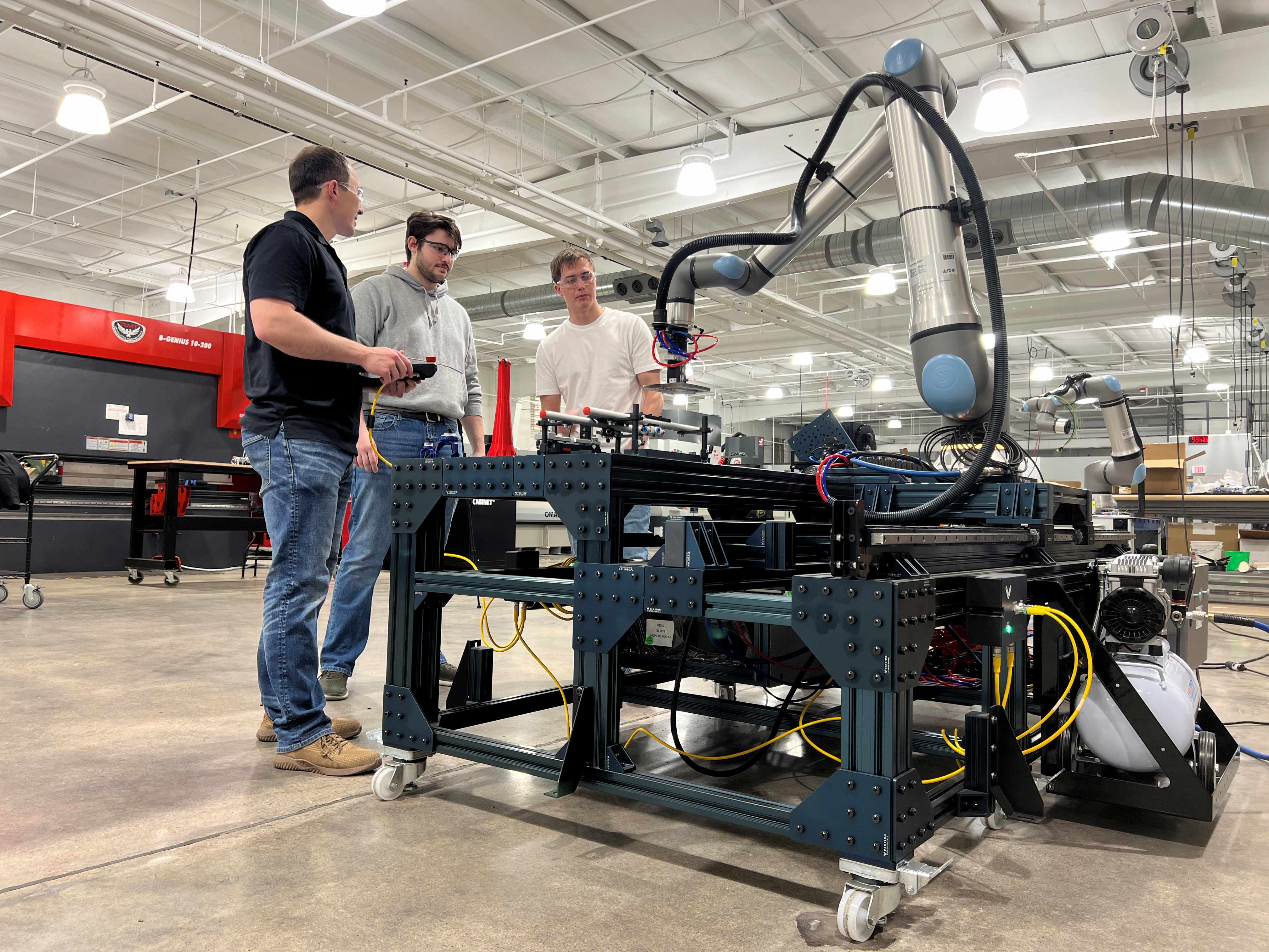 Three TDI employees working with a robotic arm and manufacturing system at the Technology Development Institute (TDI).