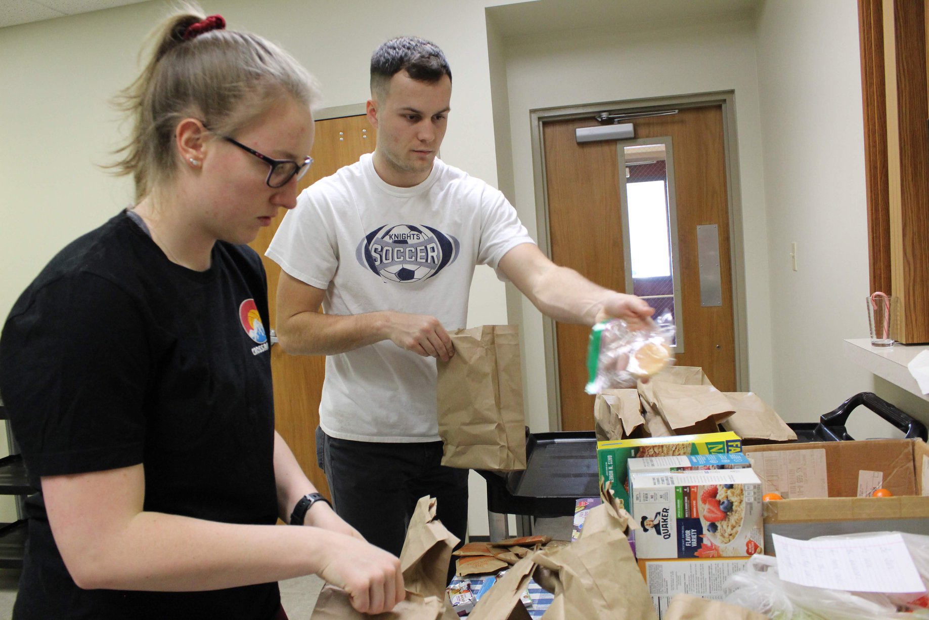 two students fulling brown paper bags with food 